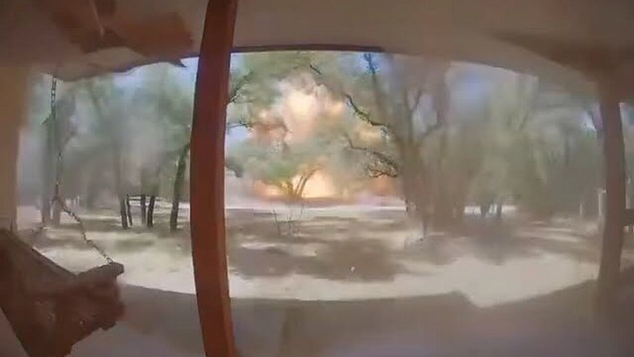Still from the video: a fireball and dust cloud erupt among the trees across the street, seen from a porch doorbell camera.